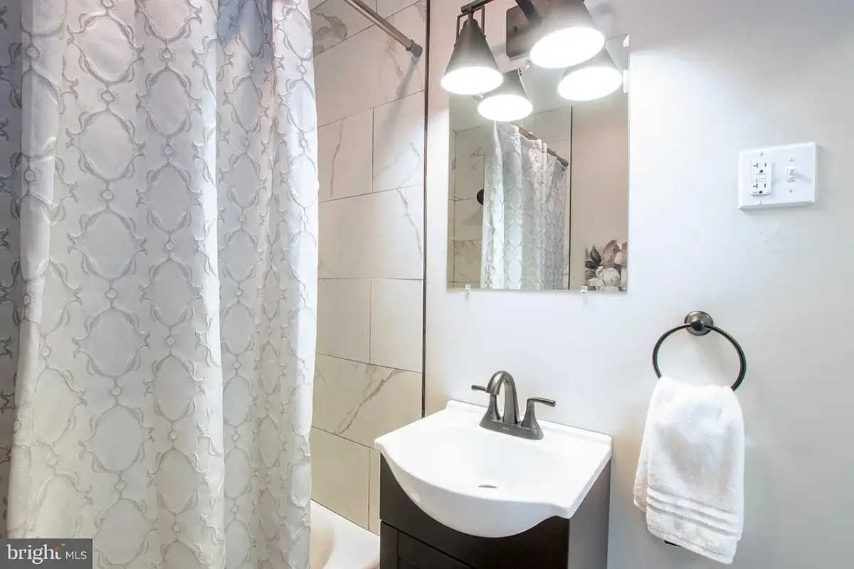 Small bathroom with shower and a white sink with a black vanity.